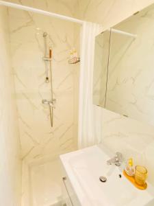 La salle de bains blanche est pourvue d'un lavabo et d'une douche. dans l'établissement Charmant studio calme, proche La Défense & Paris & JO 2024, à La Garenne-Colombes