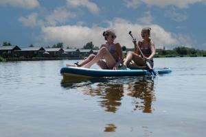 dos chicas sentadas en una tabla de paddle en el agua en Familie vakantiepark Krieghuusbelten, en Raalte