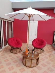 zwei rote Stühle und ein Tisch mit einem Regenschirm in der Unterkunft Appartements Andrian Location in Antananarivo