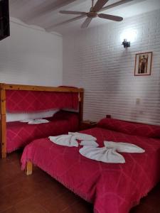 2 Betten in einem Zimmer mit roter Bettwäsche und einem Ventilator in der Unterkunft Hotel 20 de Junio in Mina Clavero