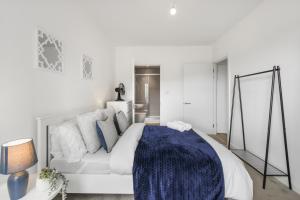 a white bedroom with a large bed with a blue blanket at Centrally Located Modern 2Bed 2Bath Apartment in London