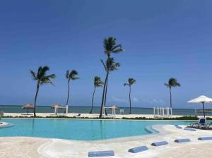 a swimming pool with palm trees and the beach at En la playa con piscina in Punta Cana
