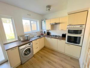 cocina con armarios blancos, lavadora y secadora en 4-Bedroom House - South London CR7, en Thornton Heath