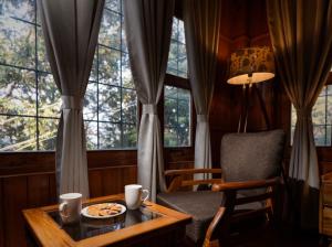 a room with a table and a chair and windows at The Manora Woods Resort - Private Hill Top, Gethiya, Nainital in Nainital