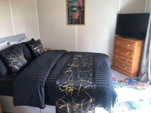 a bed with a black and gold comforter and a television at Couple’s Lodge With Hot Tub in Lincolnshire