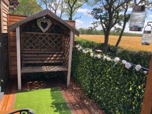 a wooden bench next to a hedge with pink roses at Couple’s Lodge With Hot Tub in Lincolnshire