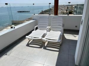Dos sillas blancas sentadas en un balcón con vistas al océano en Suite 1ra Fila Vista Bahía - 100 Metros Las Velas 601 T1 en Paracas