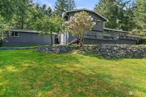 a house with a stone wall and a tree in a yard at Secluded Sanctuary With a View of The Puget Sound in Gig Harbor