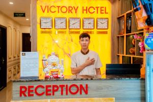 a man standing at a podium in front of a sign at Victory Hotel in Hanoi