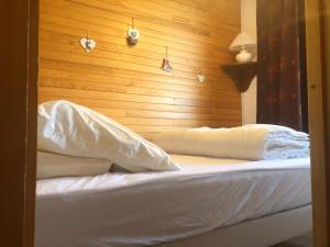 a bed with white sheets and a wooden wall at Appartement avec terrasse magnifique vue montagne in Saint-François-Longchamp
