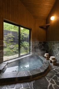 a hot tub in a room with a large window at Yufuin Yufusaryo in Yufuin