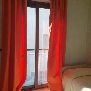 - une chambre dotée d'une fenêtre avec des rideaux rouges et d'un lit dans l'établissement Hotel Ristorante Rinelli, à Margherita di Savoia