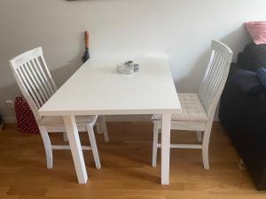 Biały stół z dwoma krzesłami i kubkiem w obiekcie Fin lägenhet med balkong centralt o bra läge w mieście Käringön