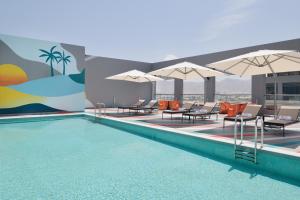 a pool with chairs and umbrellas on a building at Aloft Muscat in Muscat