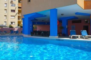 a swimming pool with blue chairs and a building at Apartamento en La Carihuela (Torremolinos) in Torremolinos