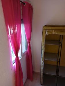 a room with a window with pink curtains and a shelf at Habitacion de matrimonio en Castilleja de la Cuesta in Castilleja de la Cuesta