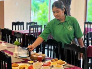 una mujer con una camisa verde preparando comida en una mesa en Ama Garden Sauraha, en Sauraha