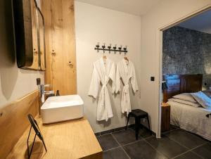 een badkamer met een wastafel en witte jassen aan een muur bij Le clos des pierres rouges in Saint-Privat-dʼAllier