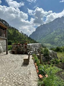 a stone patio with a building and mountains in the background at Guest House Kukaj Valbone in Valbonë