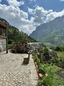 a stone patio with a building and mountains in the background at Guest House Kukaj Valbone in Valbonë