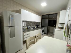 a kitchen with white cabinets and a white table and chairs at Apartamento aconchegante e espaçoso! in Guarujá