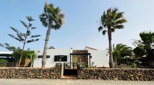 a white house with palm trees and a stone wall at Surf&fun heated pool villa in La Oliva
