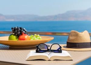 un chapeau, des lunettes de soleil et un livre sur une table avec des fruits dans l'établissement Artemis ΙnCreteble Cretan Resindences Collection, à Siteía
