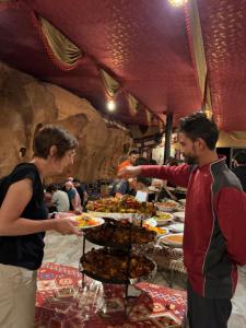 a man handing a woman a plate of food at Wadi Rum Fire Camp in Wadi Rum