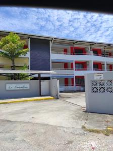 a white building with red windows and a tree at La Coraline Standing in Kourou