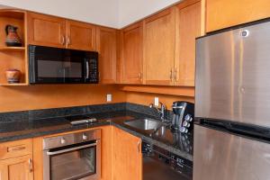 a kitchen with wooden cabinets and a stainless steel refrigerator at Alpenglow Lodge One Bedroom Penthouse by MVA in Whistler