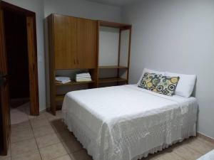 een slaapkamer met een wit bed en een houten kast bij Apart. aconchegante, 100 m da praia. in Porto Seguro