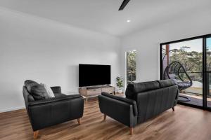 a living room with two leather chairs and a flat screen tv at Kira Lani - Pet friendly Tura in Tura Beach