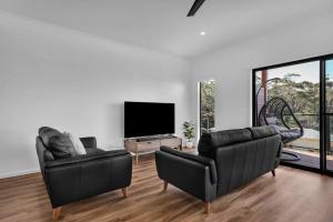 un soggiorno con 2 sedie in pelle e una TV a schermo piatto di Kira Lani - Pet friendly Tura a Tura Beach