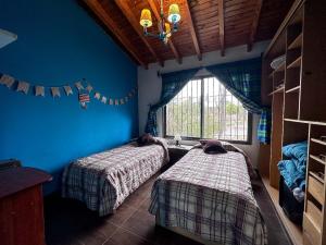 2 camas en una habitación con paredes azules y ventana en Casa en zona residencial Mendoza en Luján de Cuyo