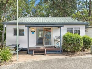 una pequeña casa blanca con un banco delante en NRMA Ocean Beach Holiday Resort en Umina