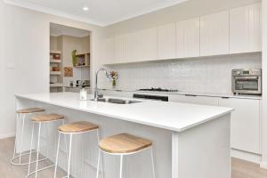 una cocina con armarios blancos y una barra con taburetes en Coolabah House - Tranquil Haven in Nulkaba, en Nulkaba