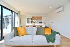 uma sala de estar com um sofá cinzento com almofadas laranja em Chatham Street - Christchurch Holiday Homes em Christchurch