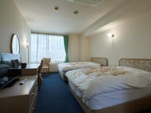 笛吹市にあるTabist Onsen Hotel Toyoのベッド2台、デスク、テレビが備わるホテルルームです。