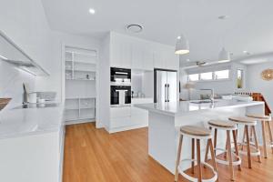 a white kitchen with bar stools and a counter at LEO2-SOPHISTICATED, BEACH HOLIDAY HOME in Alexandra Headland