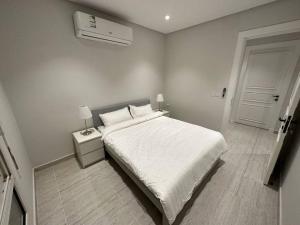 a white bedroom with a bed and a night stand at AlYasmin, S&M Luxury Apartment in Riyadh