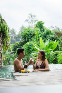mężczyzna i kobieta siedzący w basenie pijący wino w obiekcie LeRosa Valley Resort w mieście Ubud