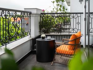 einen Balkon mit einem Tisch und einem orangen Stuhl in der Unterkunft GRAND HOTEL du LAC Hanoi in Hanoi