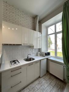 kuchnia z białymi szafkami, umywalką i oknem w obiekcie Spacious Apartment in Old City Center w Lwowie