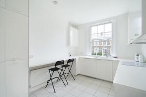 Biała kuchnia z dwoma czarnymi krzesłami w obiekcie Beautiful maisonette in the heart of Chelsea w Londynie