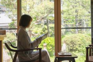 a woman sitting in a chair reading a book by a window at Kamei no Yu in Yamanouchi