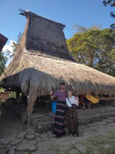 a man and a woman standing in front of a thatch hut at Lawi Luja Guest House in Kelimutu