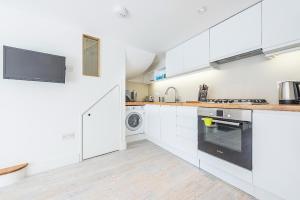 a kitchen with white cabinets and a washer and dryer at Hidden Gem in Chiswick, Stylish 1 Bedroom House in London