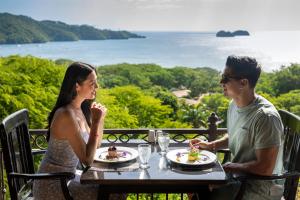 un hombre y una mujer sentados en una mesa comiendo comida en Villas Sol Beach Resort - All Inclusive en Playa Hermosa