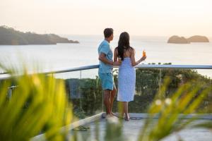 Una pareja de pie en un balcón con vistas al océano en Villas Sol Beach Resort - All Inclusive en Playa Hermosa