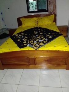 ヤウンデにあるPaulineの木製ベッド(黄色の掛け布団、白黒の毛布付)